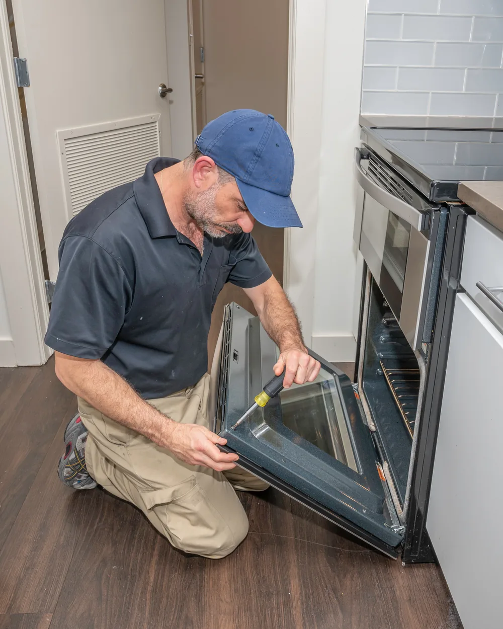 Appliance repair technician removing an oven door to service it in a home kitchen